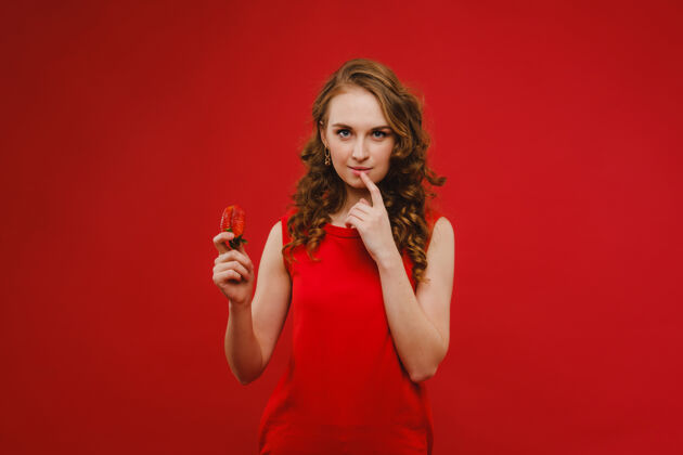 太阳镜一个穿着红色裙子 背景是红色的漂亮女孩手里拿着一个草莓 微笑着节食美味草莓