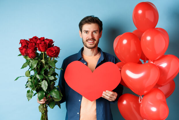 伴侣情人节浪漫男朋友带着一束红玫瑰和心形气球微笑着 在情人节约会时为爱人带上礼物 站在蓝色的背景上同性恋礼物日子