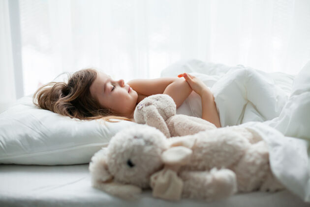 女孩可爱的小女孩睡在白色的床上 旁边放着兔子玩具小可爱可爱