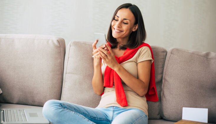 连接年轻的现代自信微笑的女人在家工作或放松 坐在沙发上用智能手机通信女人信息