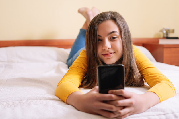 留言躺在床上拿着手机的年轻女子生活新闻喜悦