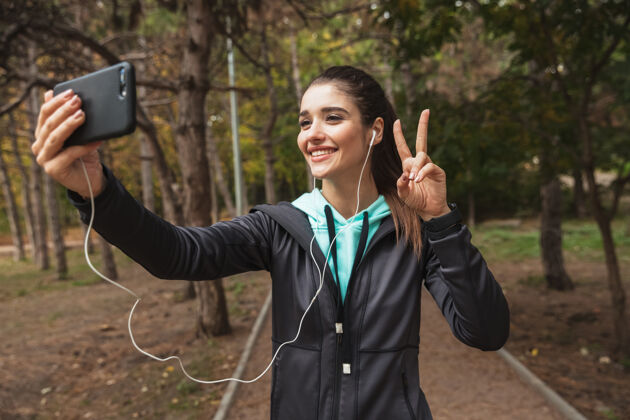 跑步微笑的健身女士戴着耳机听音乐 站在公园里自拍散步休息健身
