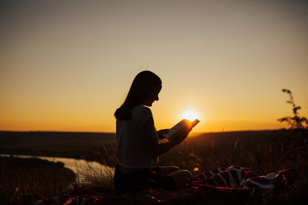 风景美丽的夕阳下 女孩在田野里看书休闲女人时间