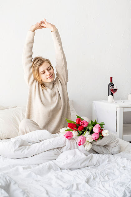 浪漫快乐的女人穿着睡衣坐在床上 愉快地享受鲜花和伸展肖像生活方式花