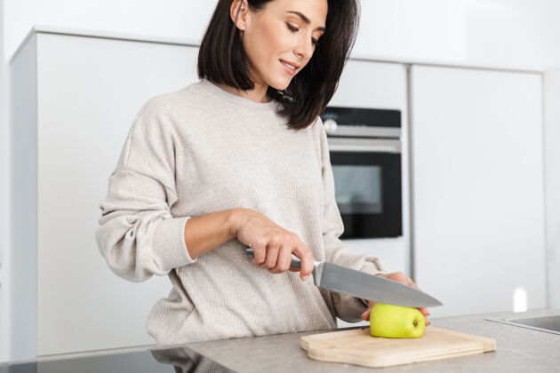 水果30多岁的漂亮女人站在家里的现代厨房里 一边用燕麦片和水果做早餐深色头发肖像舒适