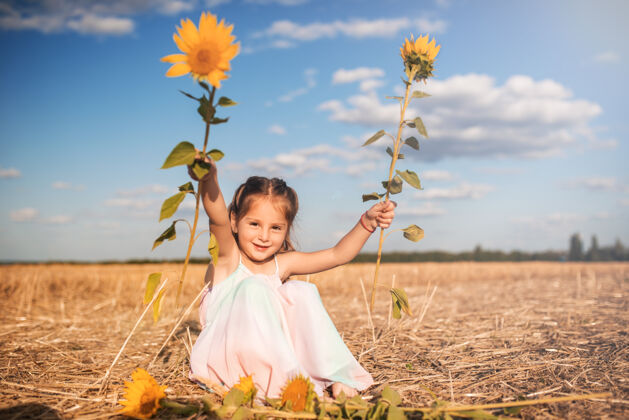 年轻穿着长太阳裙的可爱小女孩坐在地上乡村田野孩子