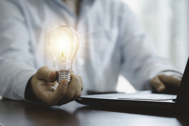 经济商人拿着发光的灯泡 用笔记本电脑输入商业战略思想 创意思维和创新理念绘画发明智能