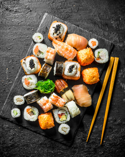 生的美味的面包卷 寿司和maki放在石头板上筷子.on黑色乡村餐桌套餐膳食蔬菜