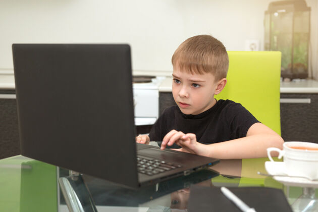 学习小男孩坐在厨房的桌子旁 手里拿着一台笔记本电脑用户学生肖像