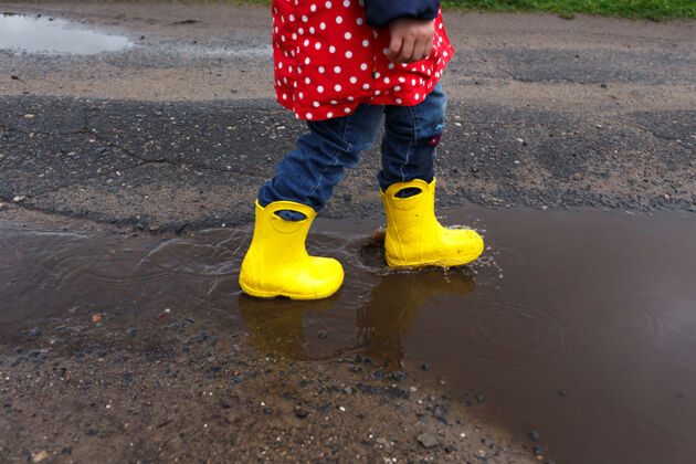 橡胶一个穿着黄色靴子的小女孩跳到了春天的水坑上 离水坑很近-起来开心童年搞笑快乐年轻