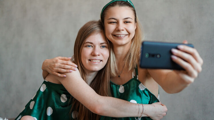 采取两个美丽快乐的女朋友在睡衣派对上用智能手机拥抱自拍朋友聚会女性