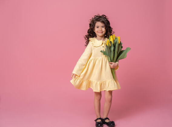 搞笑粉红工作室里一个穿着黄色连衣裙的微笑女孩背景欢快郁金香花束快乐的孩子郁金香爱小