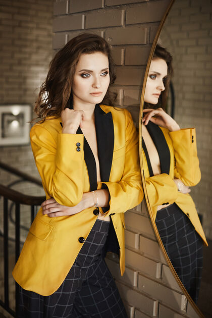 奢华时尚性感的黑发模特女郎 妆容柔和 身着时尚的金色夹克和格子裤 站在镜子旁 在室内摆造型形状长模特