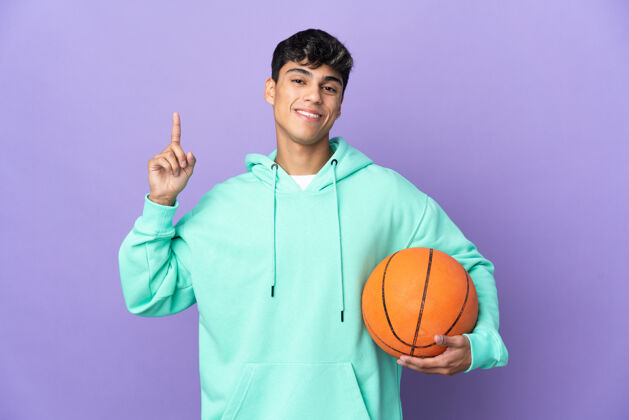 运动一个年轻人在孤零零的紫色墙壁上打篮球 举起一个手指表示最好球年轻运动