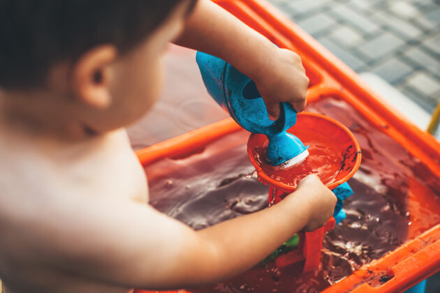 幻想一个白人男孩在外面玩水和塑料玩具的特写照片在后院被脱衣夏天水阳光