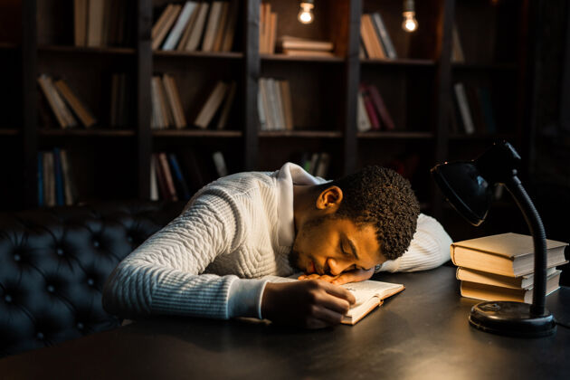 人帅气的非洲年轻人拿着书睡在桌子上教室家伙教育