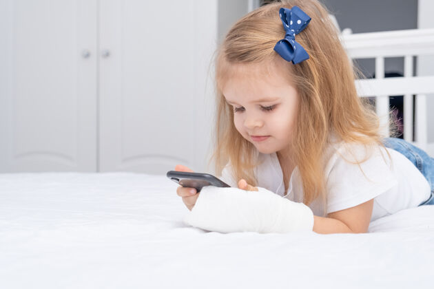 卡通手拿石膏的小女孩躺在床上用智能手机 看动画片或教育视频治疗事故石膏