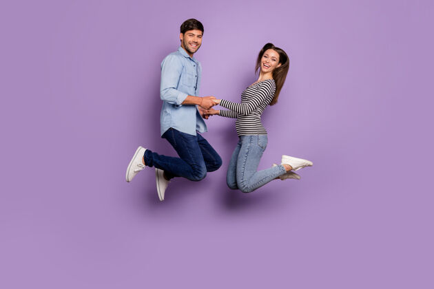 男性两个人的全长轮廓情侣搞笑的家伙女士跳高牵手友好穿着时尚休闲服装隔离粉彩紫色墙壁积极手女朋友