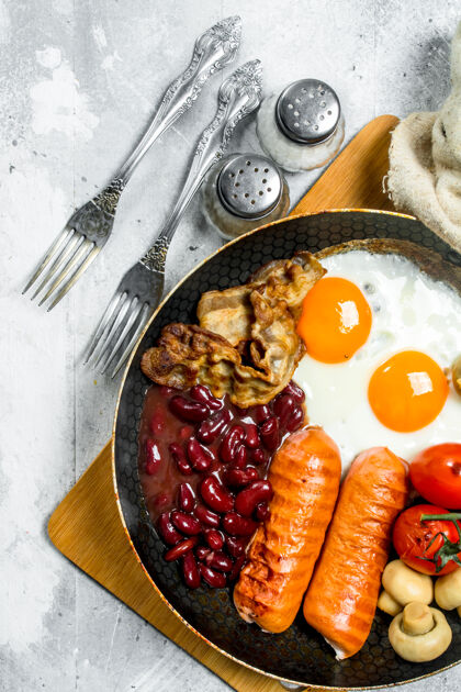 蘑菇英语早餐油炸的鸡蛋配香肠 培根和鸡蛋豆子.on质朴的表面西红柿早餐一餐