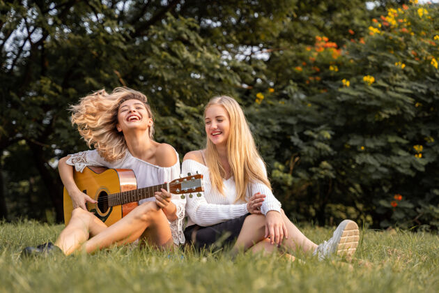 情侣画像中的白人年轻女子坐在公园外弹吉他 一起唱着幸福的歌歌手姐妹户外