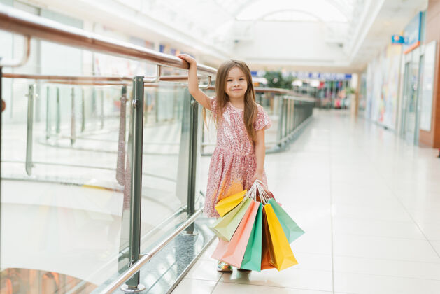 学龄前儿童商场里一个快乐的小女孩的画像一个微笑着的女孩穿着粉红色的裙子 手里拿着五颜六色的袋子 正在忙碌着购物.template为了你的广告零售童年控股
