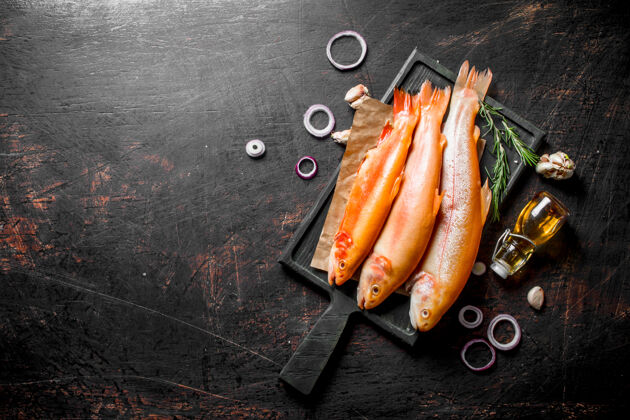 配料生鳟鱼 洋葱圈和大蒜放在深色的乡村餐桌上膳食黑暗新鲜