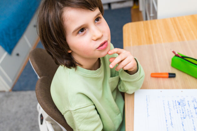 房间小男孩坐在桌子旁做作业家集中思考任务的孩子兴趣.家庭教育教育冷静人学者