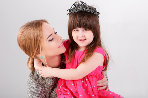 美丽美丽的小女孩穿着粉色公主裙 头戴皇冠 美丽的母亲在灰色背景下拥抱着女人甜蜜公主
