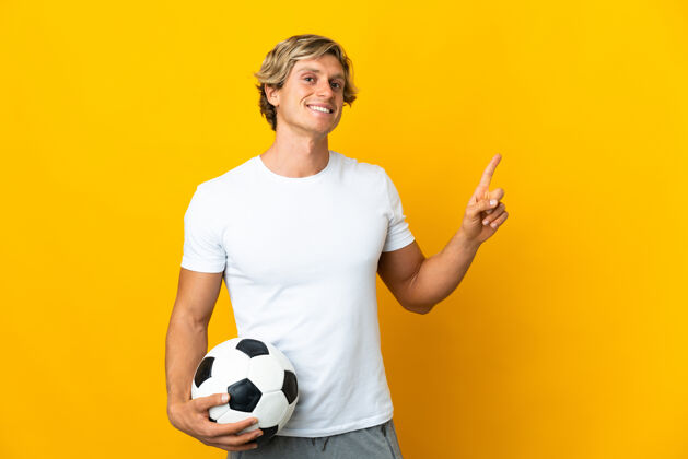 英国英国足球运动员在孤立的黄色背景下展示并举起一个手指表示最好休闲拇指运动装