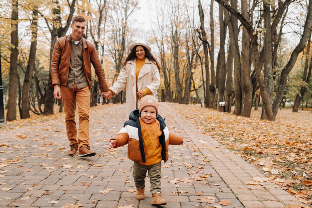 户外爸爸和妈妈带着儿子在秋天的公园里散步一家人在金秋的自然公园里散步秋天公园树叶户外