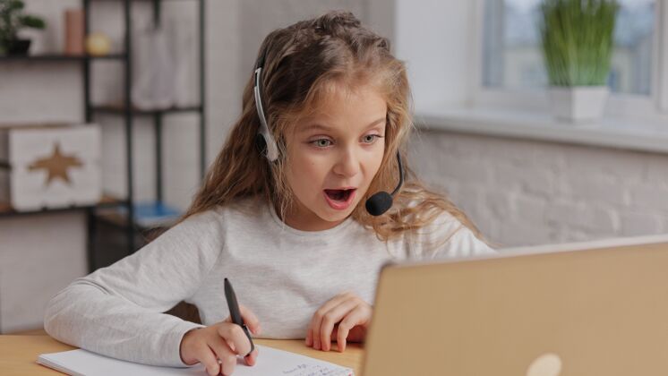 孩子一脸震惊表情的女学生打视频电话老师可爱小学女生在家用笔记本电脑学习居家耳机计算机