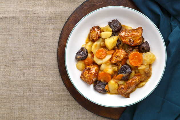 家禽犹太料理在亚麻布表面的圆板上放一个白色盘子 里面放着胡萝卜 枣子和火鸡肉葡萄干自然蜂蜜