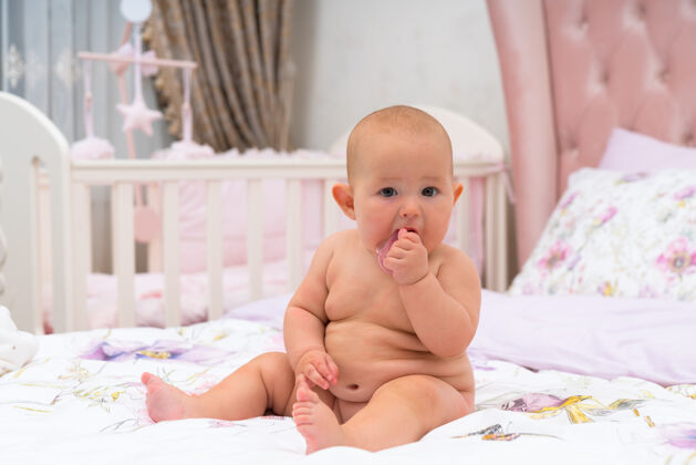 吸收一个可爱的 胖乎乎的裸体婴儿在一间有婴儿床的粉色儿童房里看着摄像机肖像婴儿床婴儿