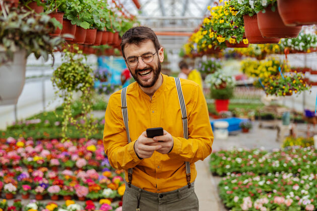 无线微笑的园丁站在温室里 通过智能手机接受顾客的订单创新花园业主