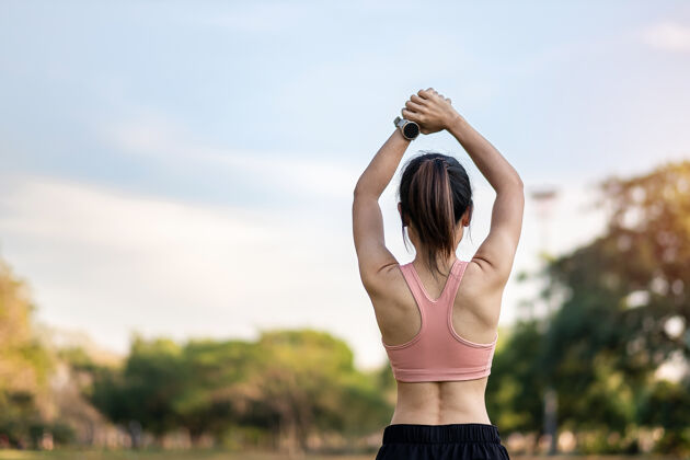 锻炼穿着粉色运动服的年轻成年女性在公园户外伸展肌肉 运动女性热身准备跑步和慢跑早上好健康 健身 运动和工作生活平衡概念减肥健身减肥