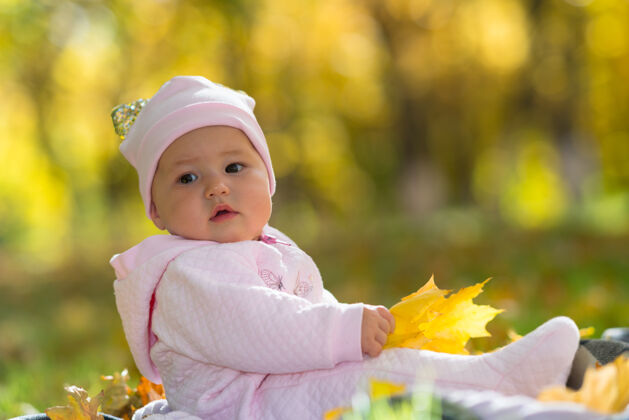 高角度一个穿着粉红色衣服的婴儿坐在黄色的秋天里 公园里的落叶树叶女孩女儿