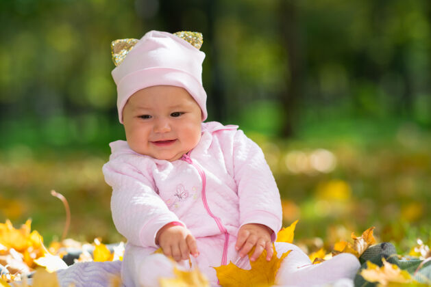 新生儿可爱的小女婴在秋天的公园里玩着五颜六色的树叶 她坐在草地上的小地毯上 低角度观看毯子可爱小