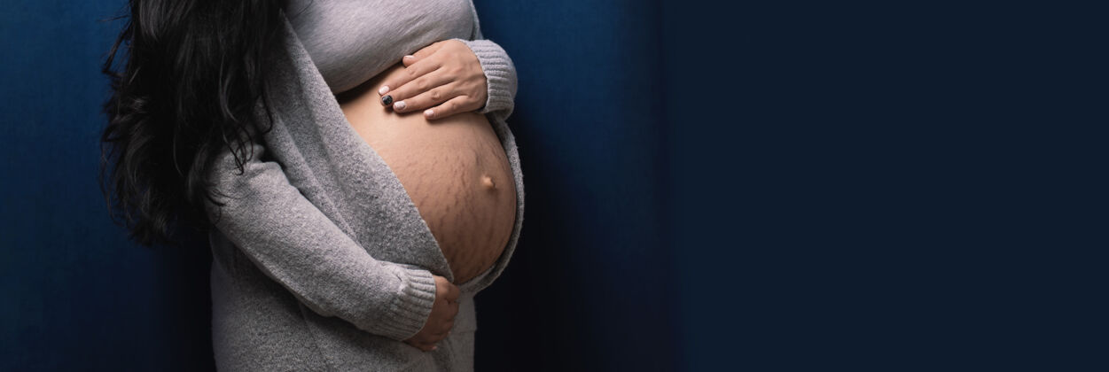 等待年轻孕妇在蓝色背景上触摸腹部 婴儿等待概念期望肚子产妇