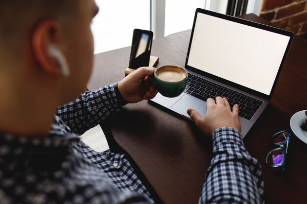 办公室拿着一杯咖啡和耳机在笔记本电脑前工作的男人家模糊背景高高质量的照片设备人屏幕