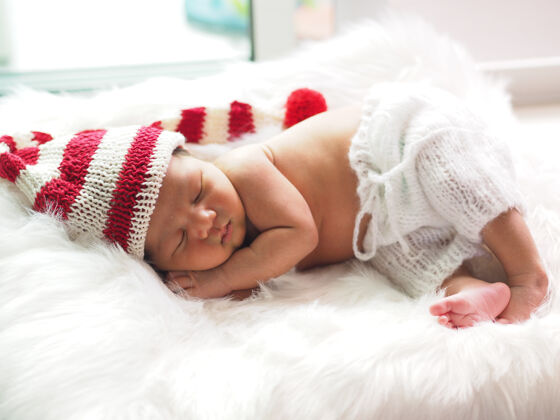 针织帽子亚洲新生婴儿戴着一顶编织的圣诞精灵帽睡在白色皮毛上小白色皮毛婴儿睡眠