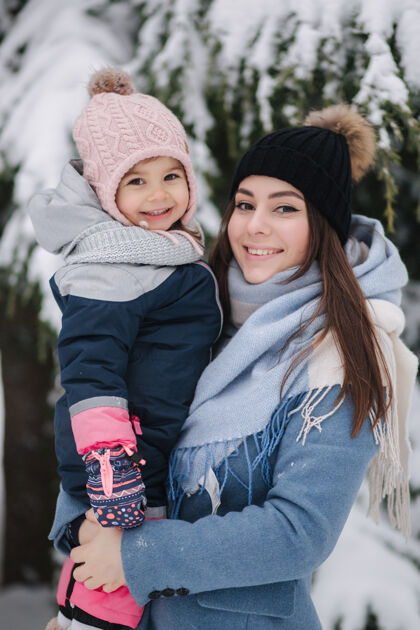 雪橇美丽的年轻妈妈和她可爱的女儿在冬季公园拉骑享受