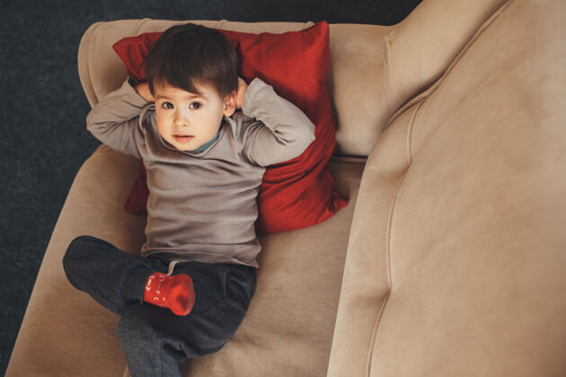 幼儿上图：一个白人男孩躺在沙发上仰望镜头休闲看沙发