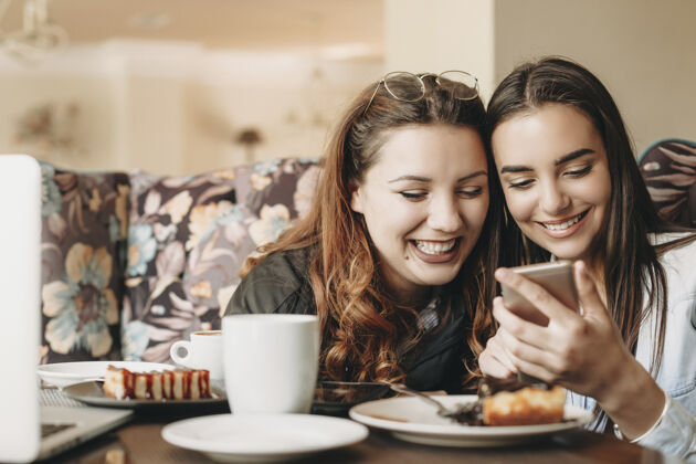 饮食可爱的大码红发女性在咖啡馆里看着智能手机 和她的女性朋友一起欢笑食物在线影响者