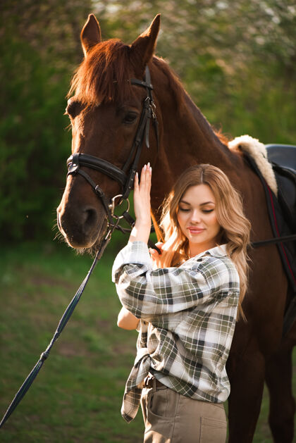 骑手美丽的姑娘牵着她的马和美丽温暖的夕阳在春天的森林里青少年户外马