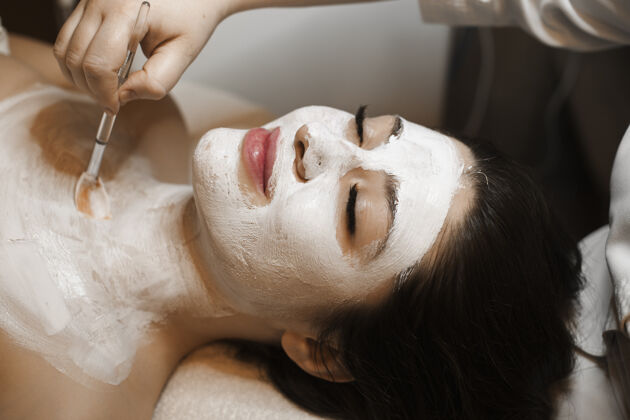 清洁一位美丽的女性斜倚在床上 闭着眼睛在脸上和脖子上做一个白色面具的侧视图漂亮人护理