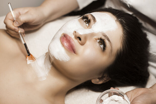 清洁一位可爱的女性在温泉度假胜地脸上戴着白色护肤面膜的特写镜头泥治疗健康