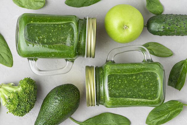 饮料绿色健康排毒冰沙与新鲜蔬菜和水果在罐子混凝土背景.平坦躺着查看健康排毒早餐概念混合罐子鳄梨