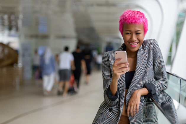 城市年轻叛逆的亚洲女商人的肖像 粉红色的头发在城市户外的人行天桥上使用信息连接