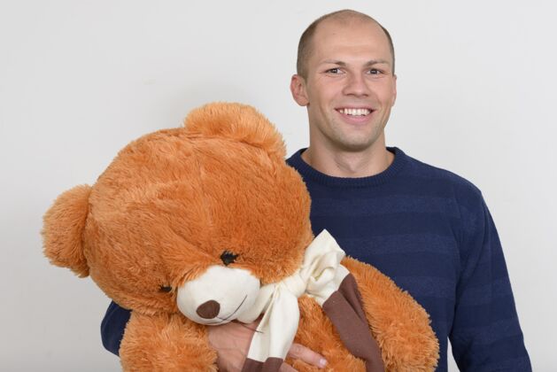 秃头快乐的年轻英俊的秃头男子手持大泰迪熊的画像泰迪大男