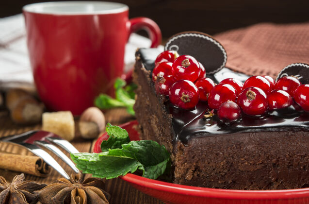 特写在红色杯子的背景上装饰着红醋栗的巧克力蛋糕的特写镜头薄荷糕点木背景